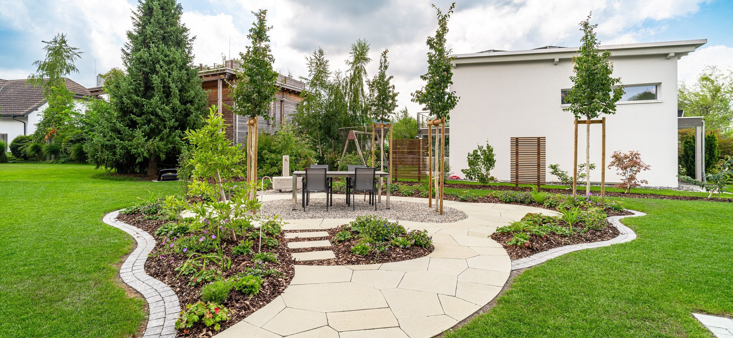 sandstein_mosaikpolatten_mit_frieda_pflasterstein_als_randabschluss_bäume_als_schattenspender