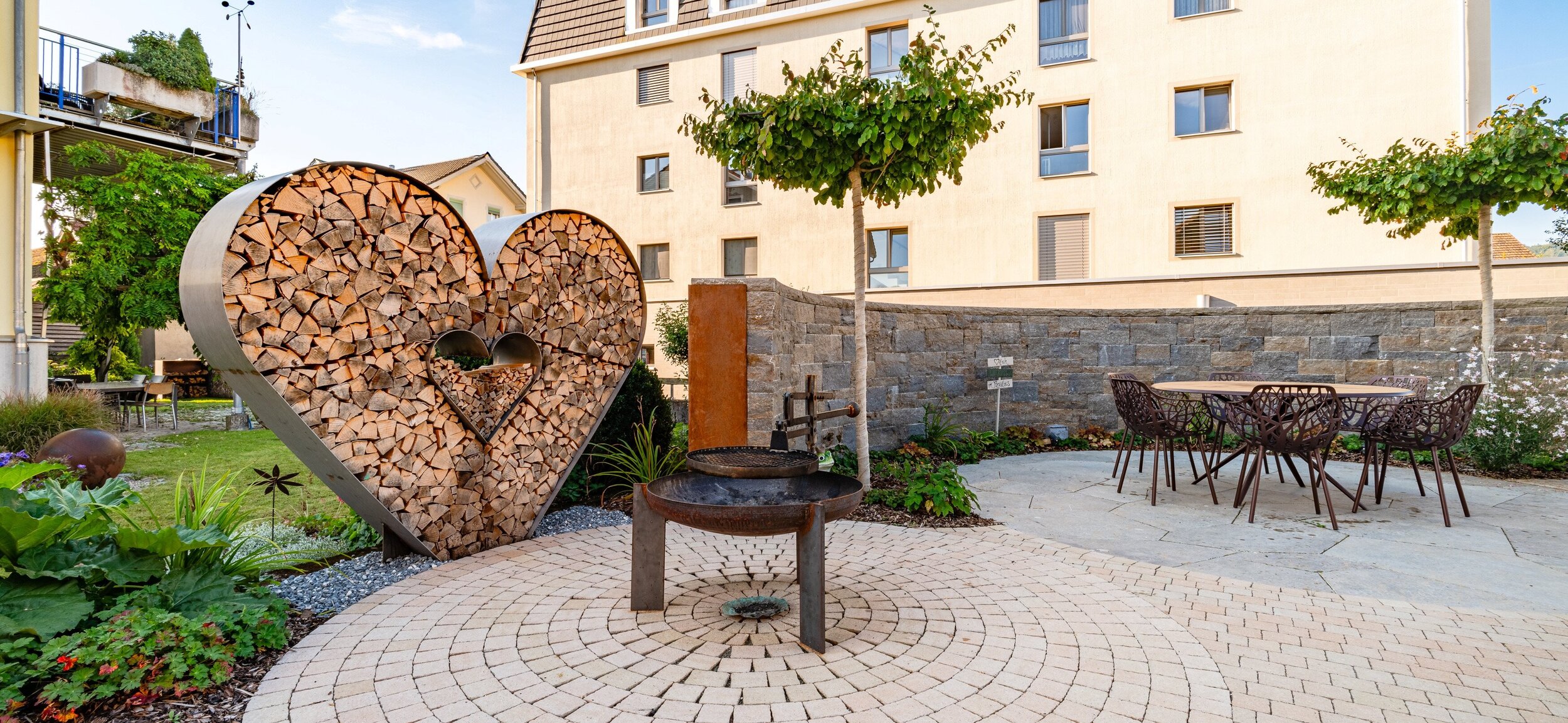 sitzplatz_mit_mauer_aus_muschelkalk_und_holzlager_in_herzform