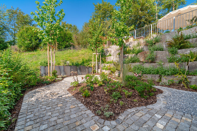 gepflasterter_gartenweg_mit_pflanzenbeeten_und_natursteinmauer_in_hanglage