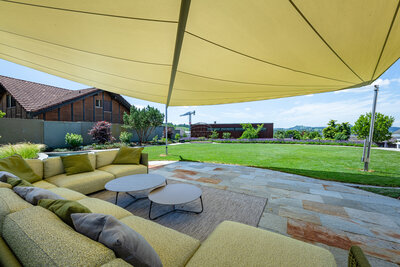 gemütlicher_loungebereich_unter_sonnensegel_mit_ausblick_auf_grünen_garten_und_modernes_haus