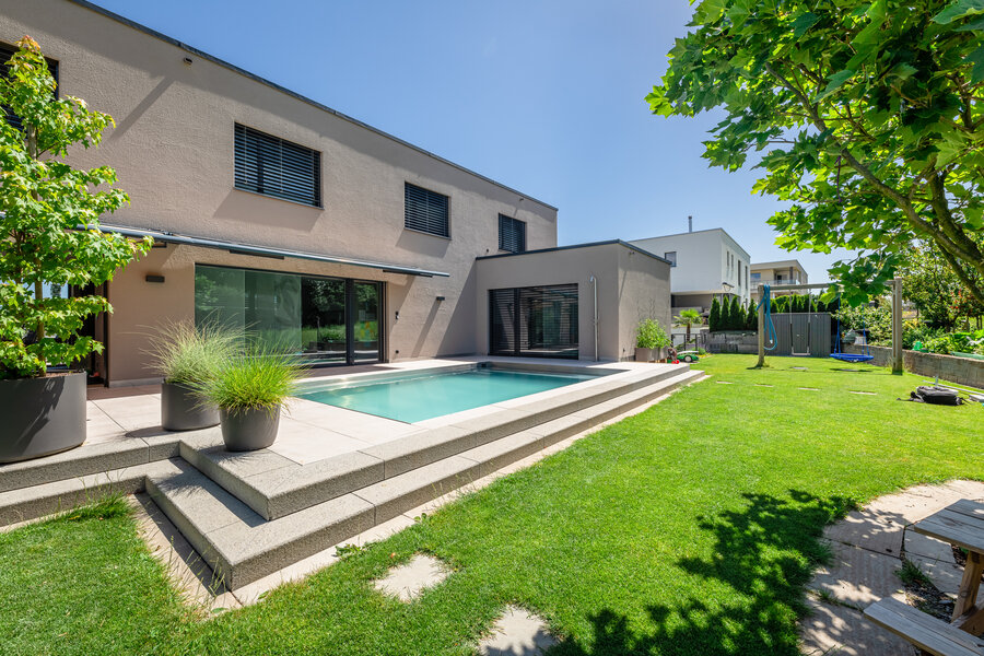 moderner_garten_mit_pool_terrasse_gartenplatte_feinsteinplatten_grüner_wiese_und_schattenspendenden_bäumen