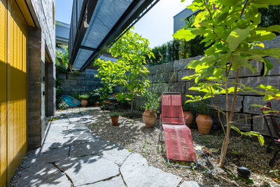 kleiner_innenhof_mit_schattenspendendem_dach_sitzbereich_pflanzen_und_steinboden_mosaikplatte_naturstein_schattenbaum