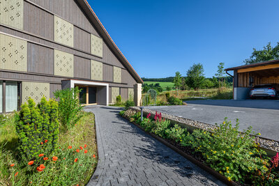 modern_hausfassade_mit_pflasterweg_frieda_begrenzung_von_gartenpflanzen_und_rotblühenden_mohnblumen