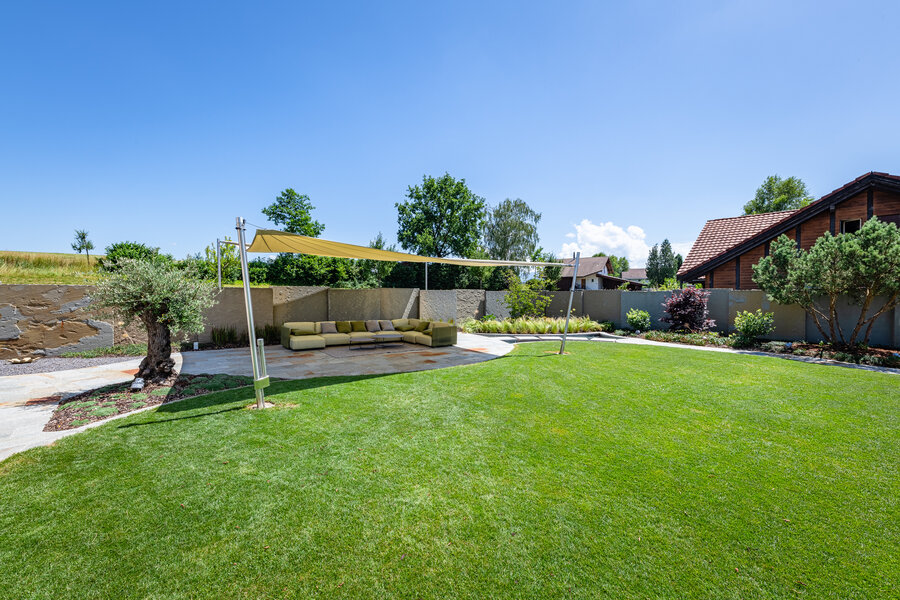 garten_mit_rasenfläche_und_geselliger_sitzgelegenheit_unter_sonnensegel_und_natursteinplatten_aus_luserna