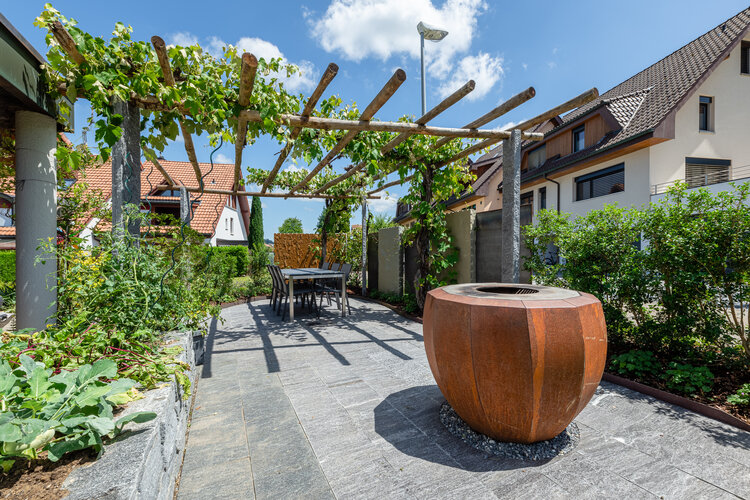 garten_mit_essbereich_und_pergola_überwachsen_mit_reben_und_feuerschale_aus_metall
