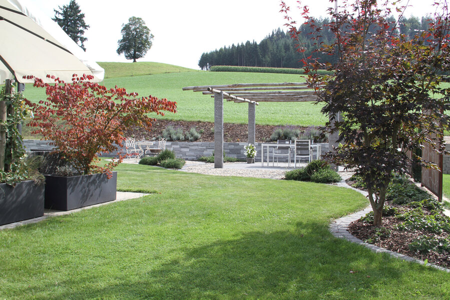garten_mit_essbereich_und_pergola_umgeben_von_grünem_terrain_und_bepflanzung