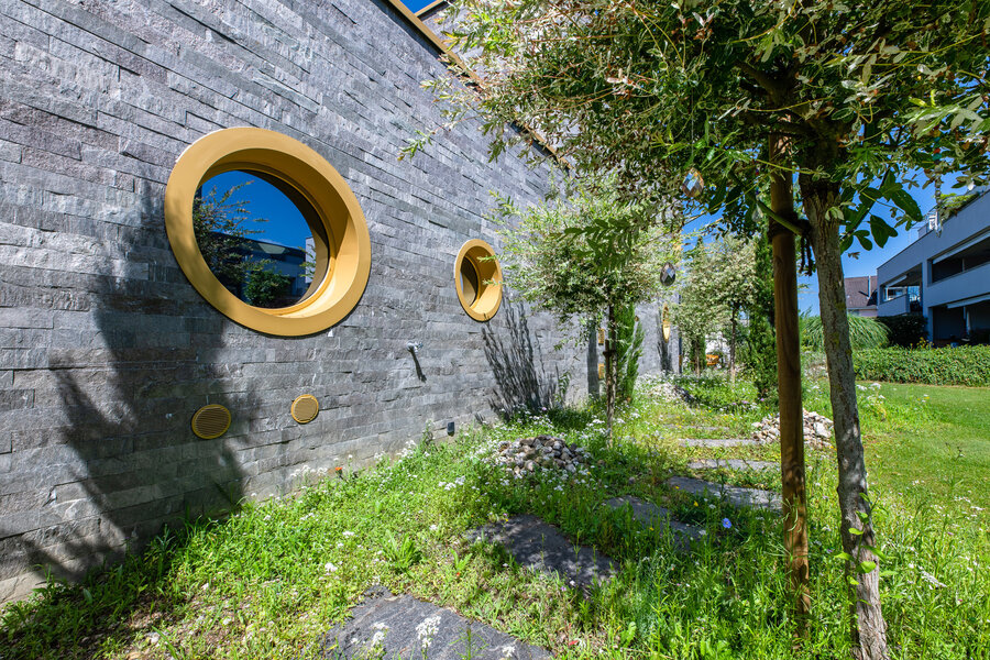 garten_mit_steinerner_wand_und_runden_fenstern_umgeben_von_bäumen_und_grünem_terrain