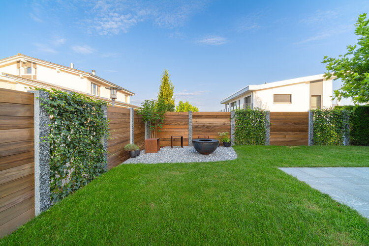 Sichtschutz_im_garten_mit_feuerstelle_und_kiesplatz_hinter_grünem_rasen