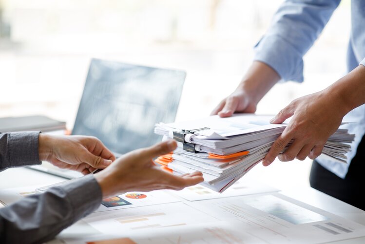 papierstapel_überreicht_an_andere_im_büro