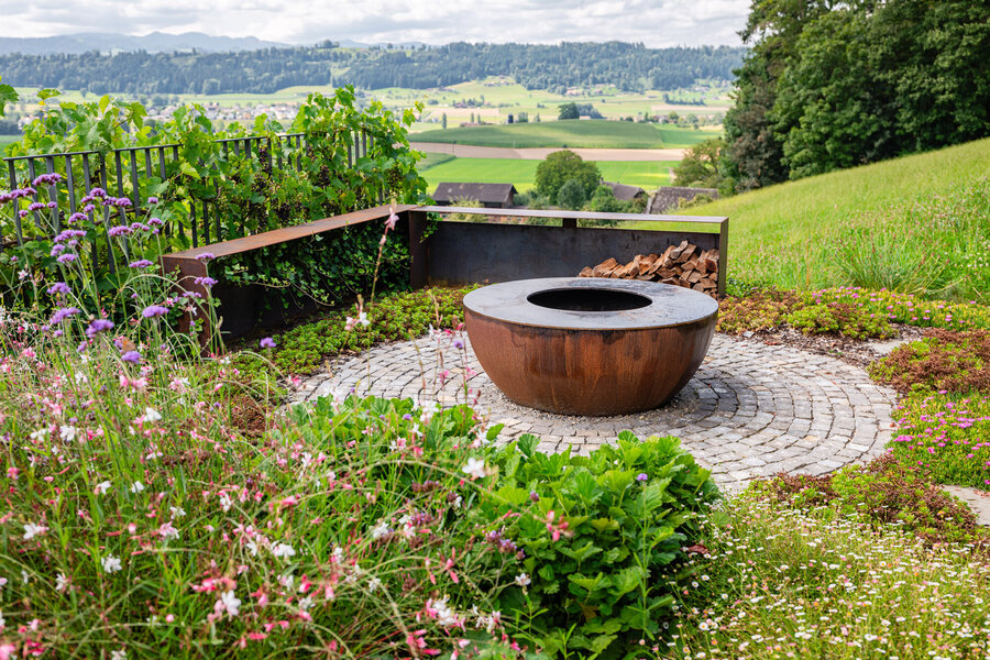 garten_mit_rustikalem_feuerstelle_und_blühenden_pflanzen_umgeben